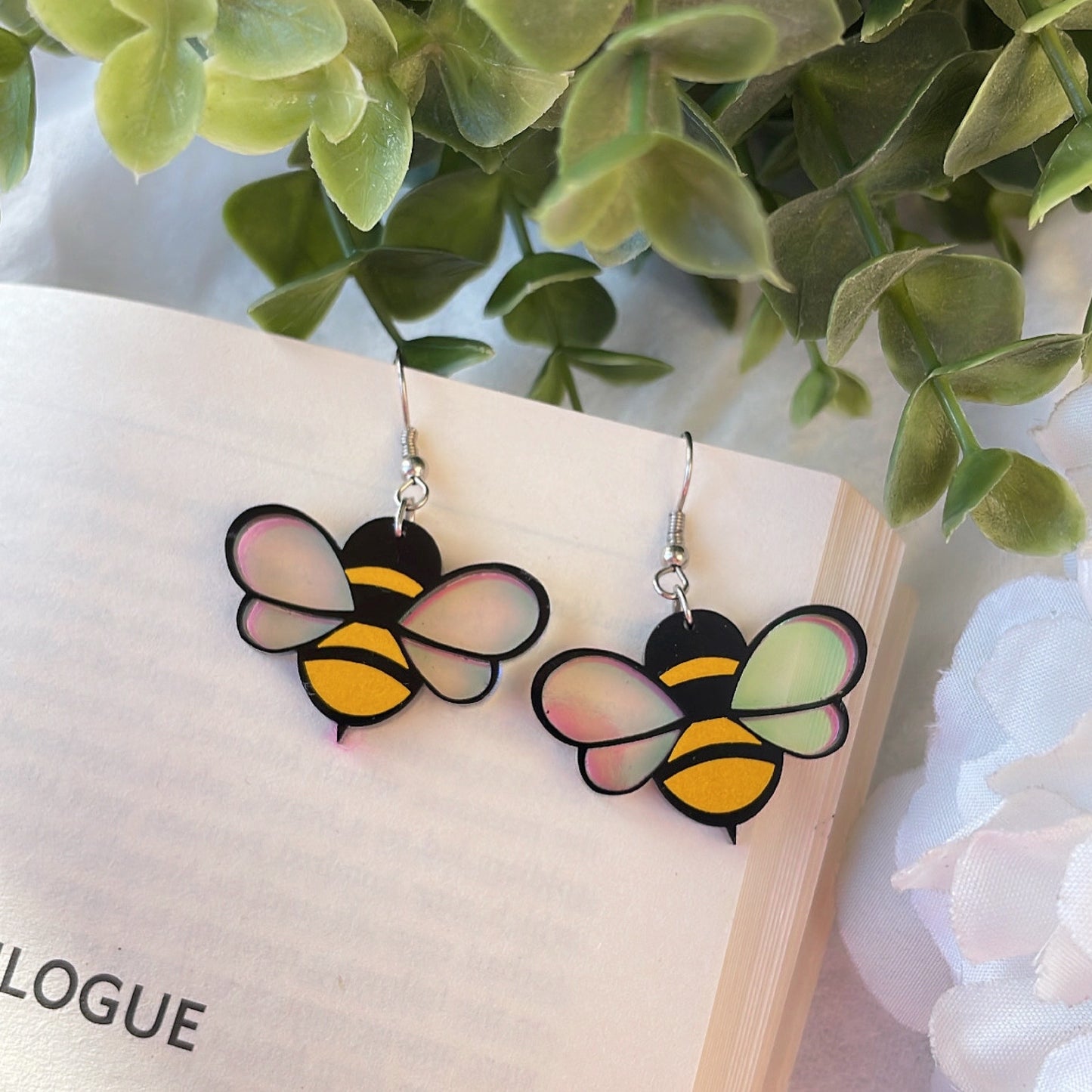 Baby Bee Earrings - Yellow and Black with a Holographin Effect - Nian by Nidhi - placed in a white and green background