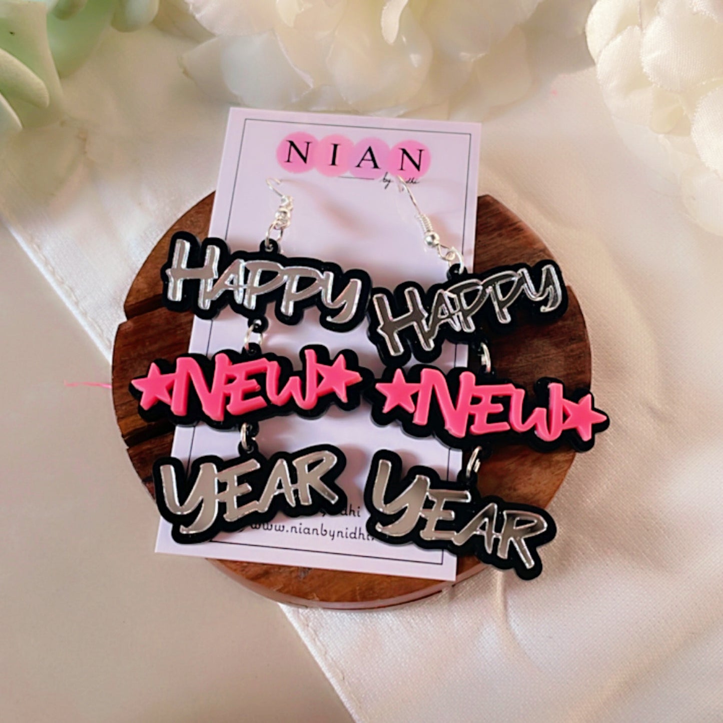 Happy New Year Earrings - Pink and Silver - Nian by Nidhi - placed in a white flowery background