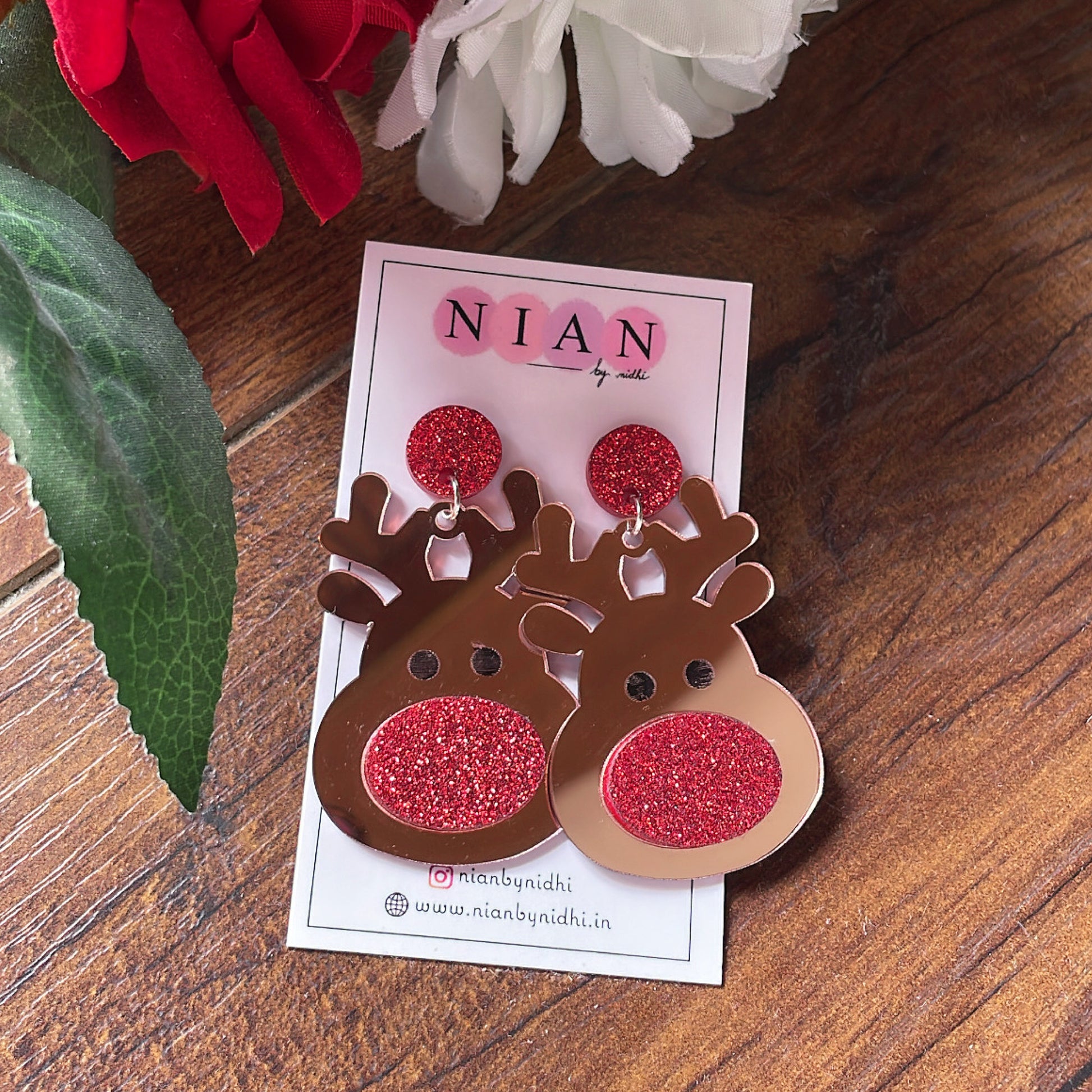 Red Rudolph Earrings - Rosegold and Red- Nian by Nidhi - placed in a brown and flowery background