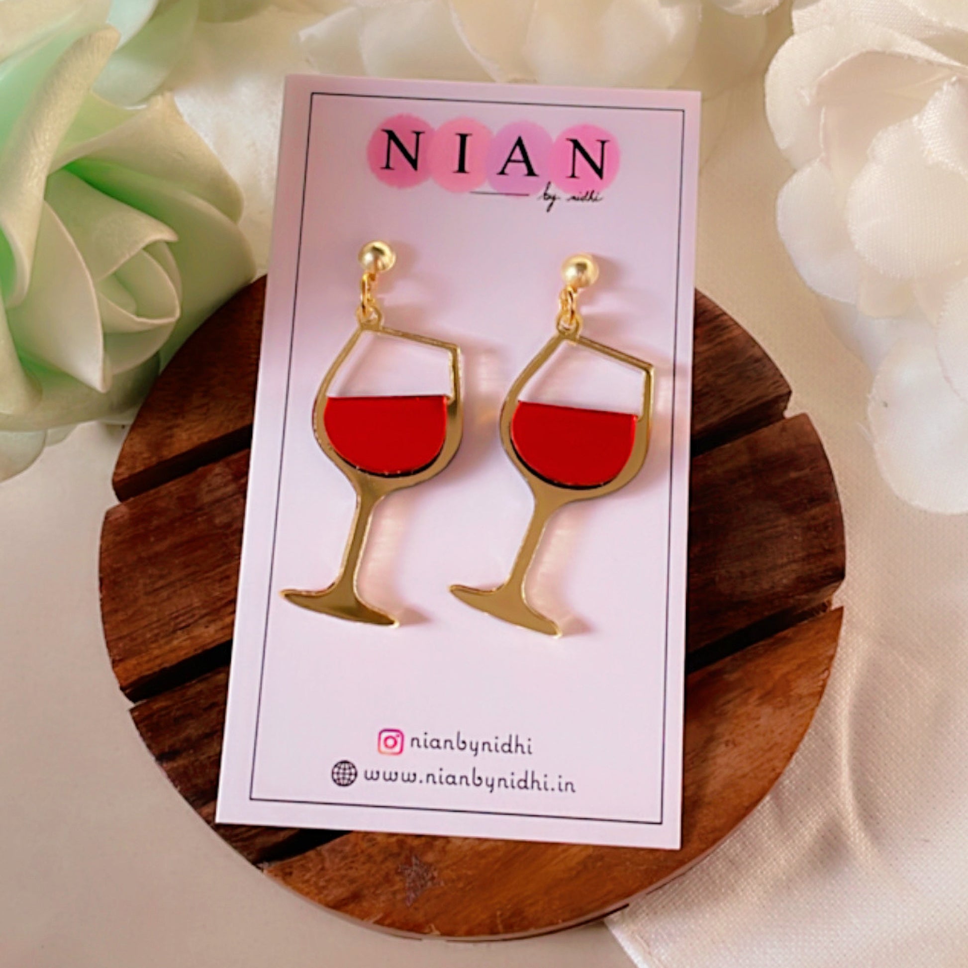Wine Goblet Earrings - Glossy Red and Golden - Nian by Nidhi - placed in a white flowery background