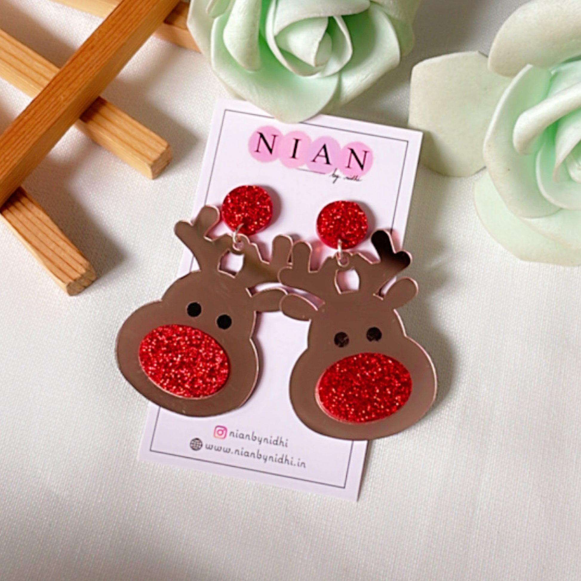 Red Rudolph Earrings - Rosegold and Red - Nian by Nidhi- placed in a brown and flowery background