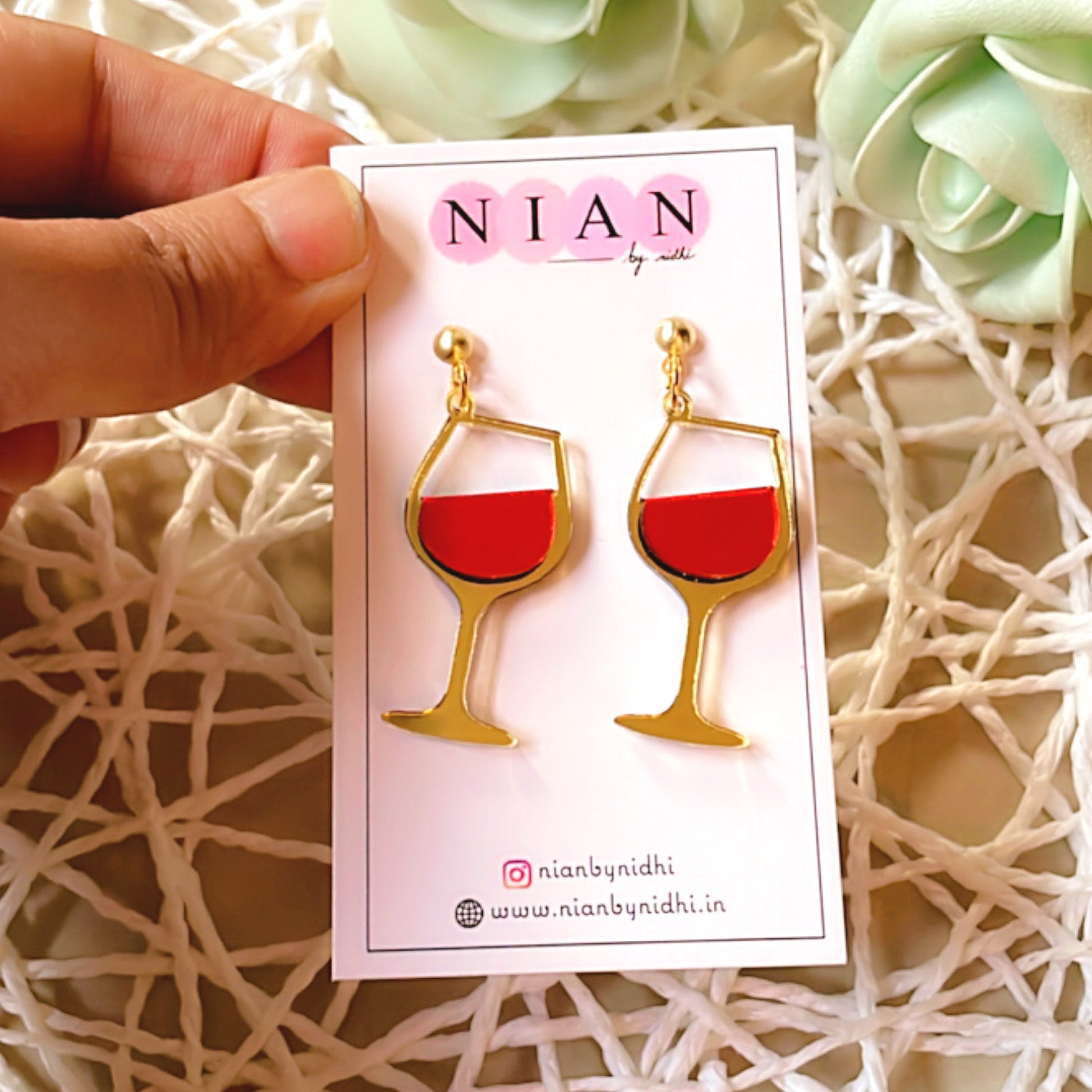 Wine Goblet Earrings - Glossy Red and Golden - Nian by Nidhi - placed in a net basket-y background, held in a hand by a woman
