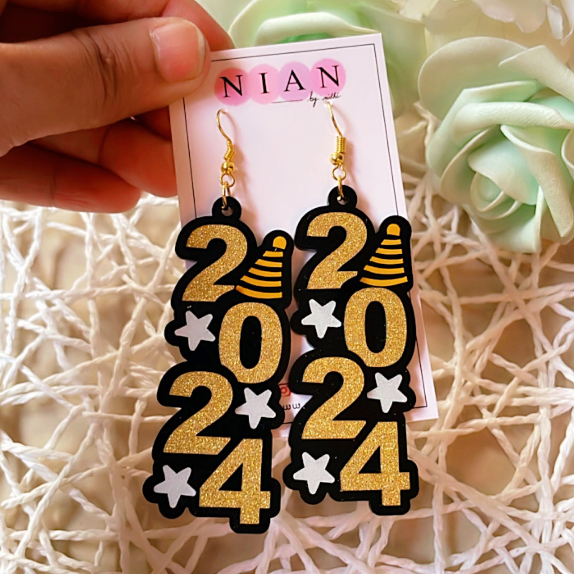 ⁠2024 Danglers - Shimmer Golden and White - Nian by Nidhi - placed in a net basket-y background, held in a hand by a woman