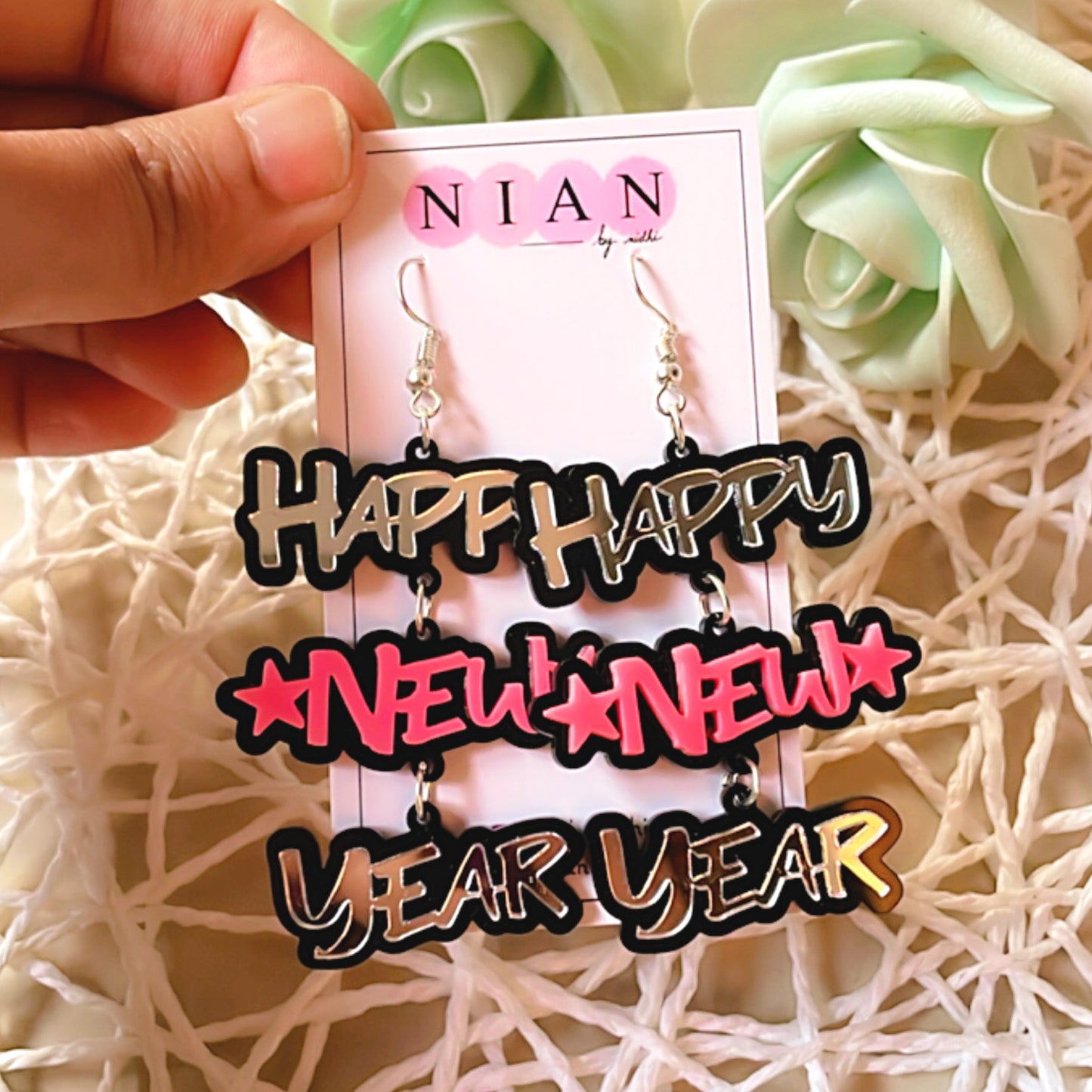 Happy New Year Earrings - Pink and Silver - Nian by Nidhi - placed in a net basket-y background, held in a hand by a woman