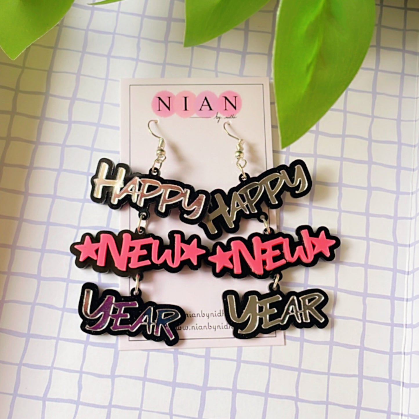 Happy New Year Earrings - Pink and Silver - Nian by Nidhi - placed in a squared-check background