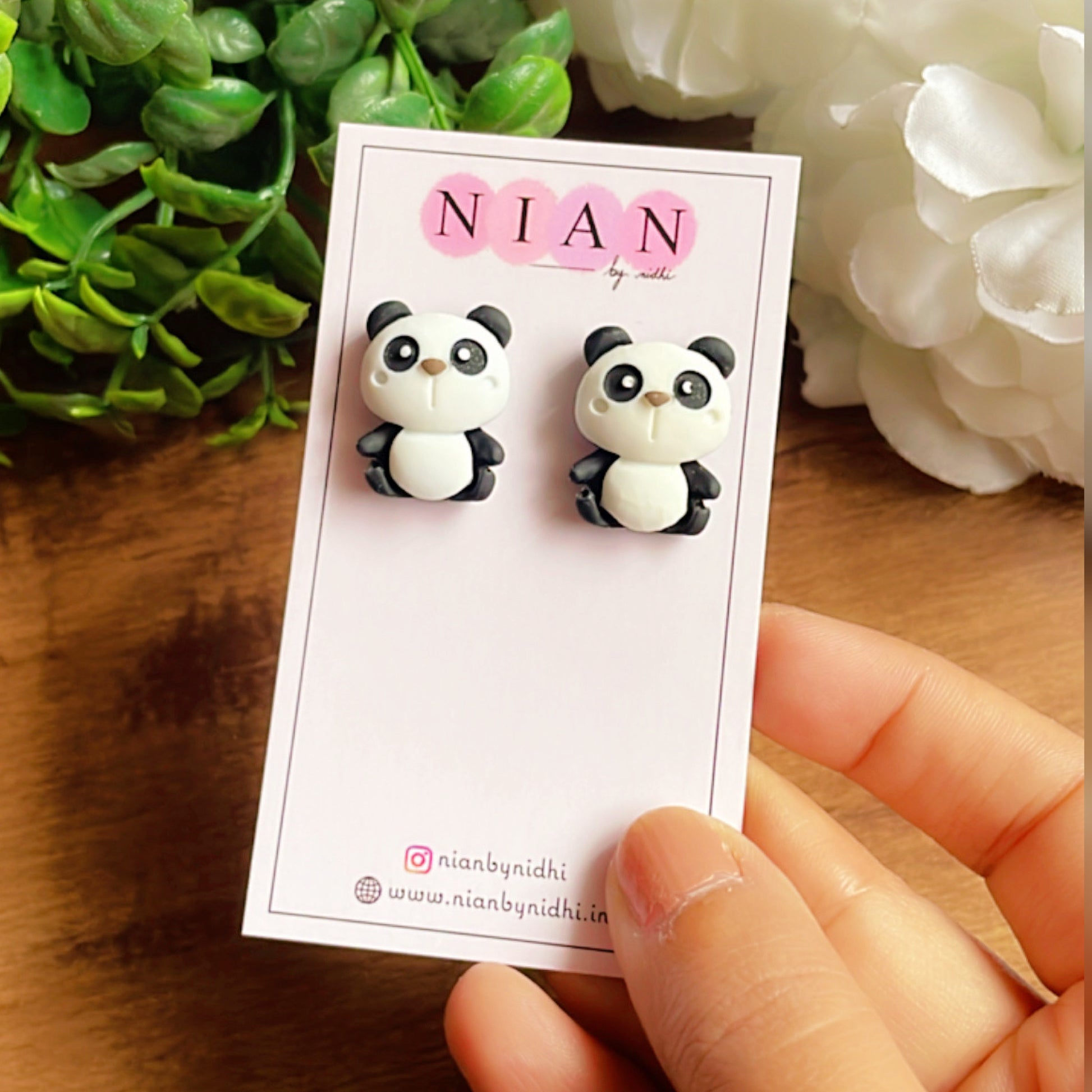 Perky Panda Studs - White and Black - Nian by Nidhi - placed in a white, brown, and green background, held in a hand