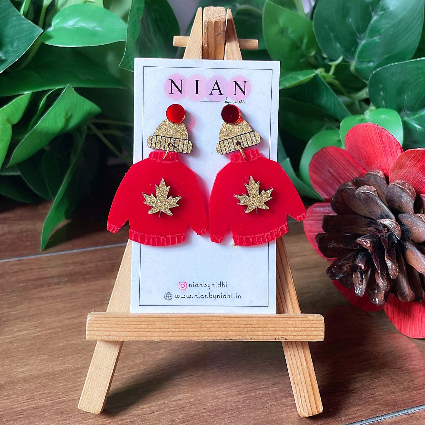 Wool Wrap Earrings - Red and Shimmer Golden - Nian by Nidhi - placed on a small wooden canvas, with a green leafy background