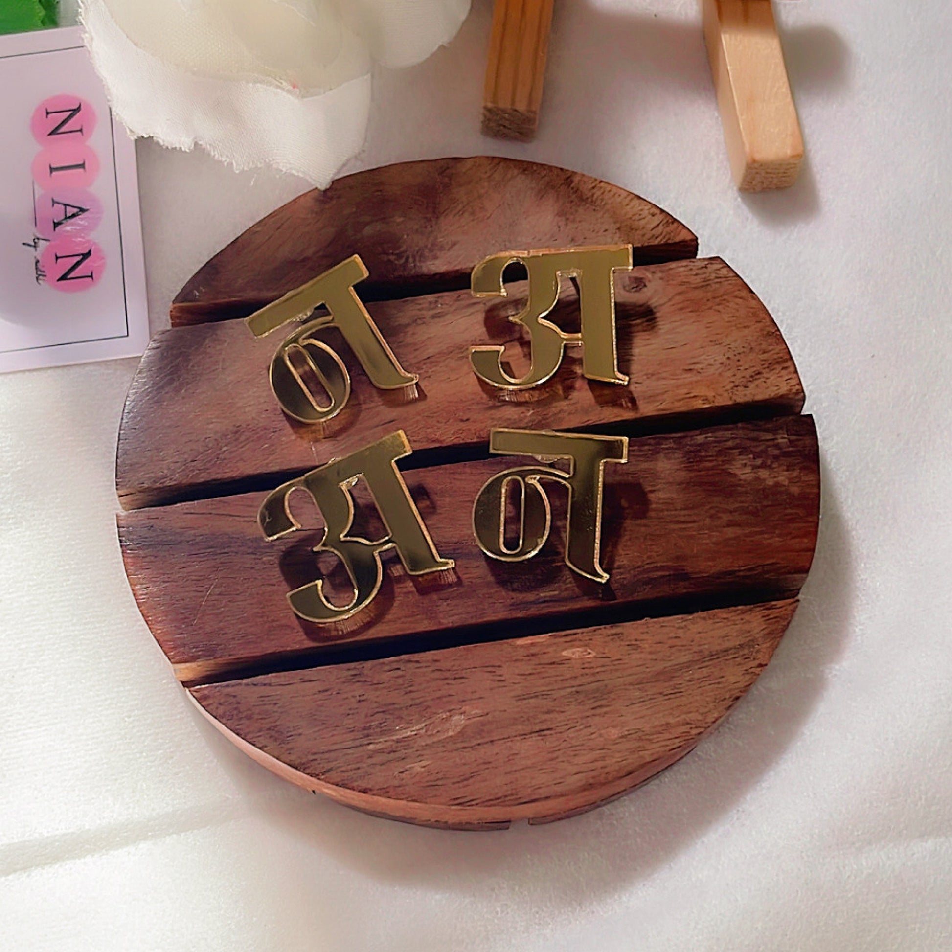 Customised Hindi Initial Studs - Glossy Golden - Nian by Nidhi - placed in a white and brown background
