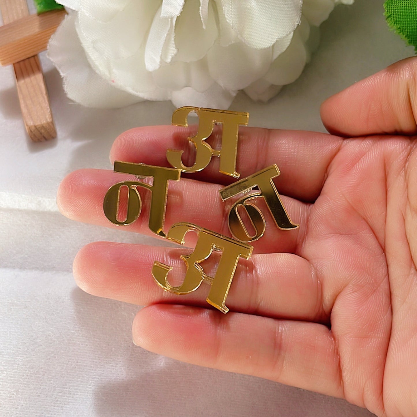 Customised Hindi Initial Studs - Glossy Golden - Nian by Nidhi - placed on a woman's hand in a white background