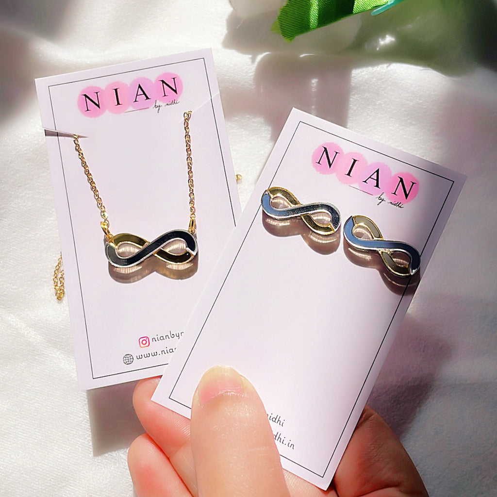 Infinity Combo (Set of 2) - Glossy Golden and Silver - Nian by Nidhi - comprises two products - Infinity Necklace and Infinity Studs - placed in a white and green background