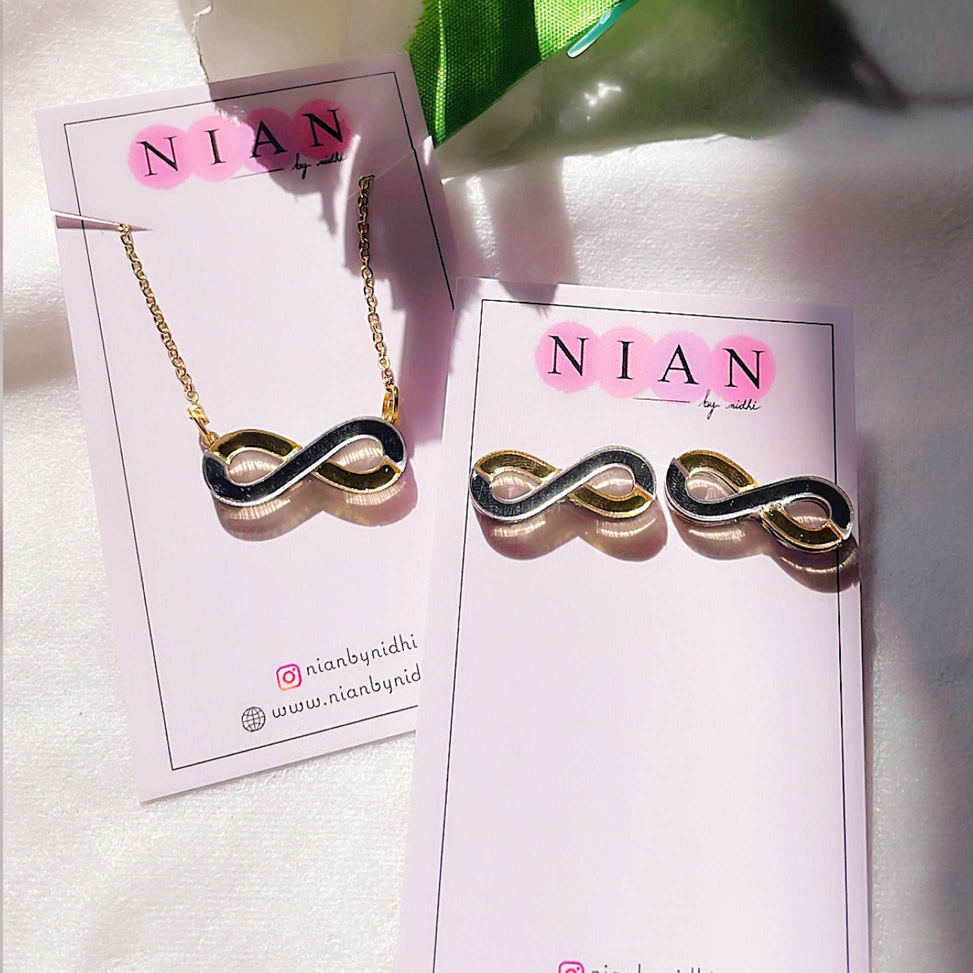 Infinity Combo (Set of 2) - Glossy Golden and Silver - Nian by Nidhi - comprises two products - Infinity Necklace and Infinity Studs - placed in a white and green background