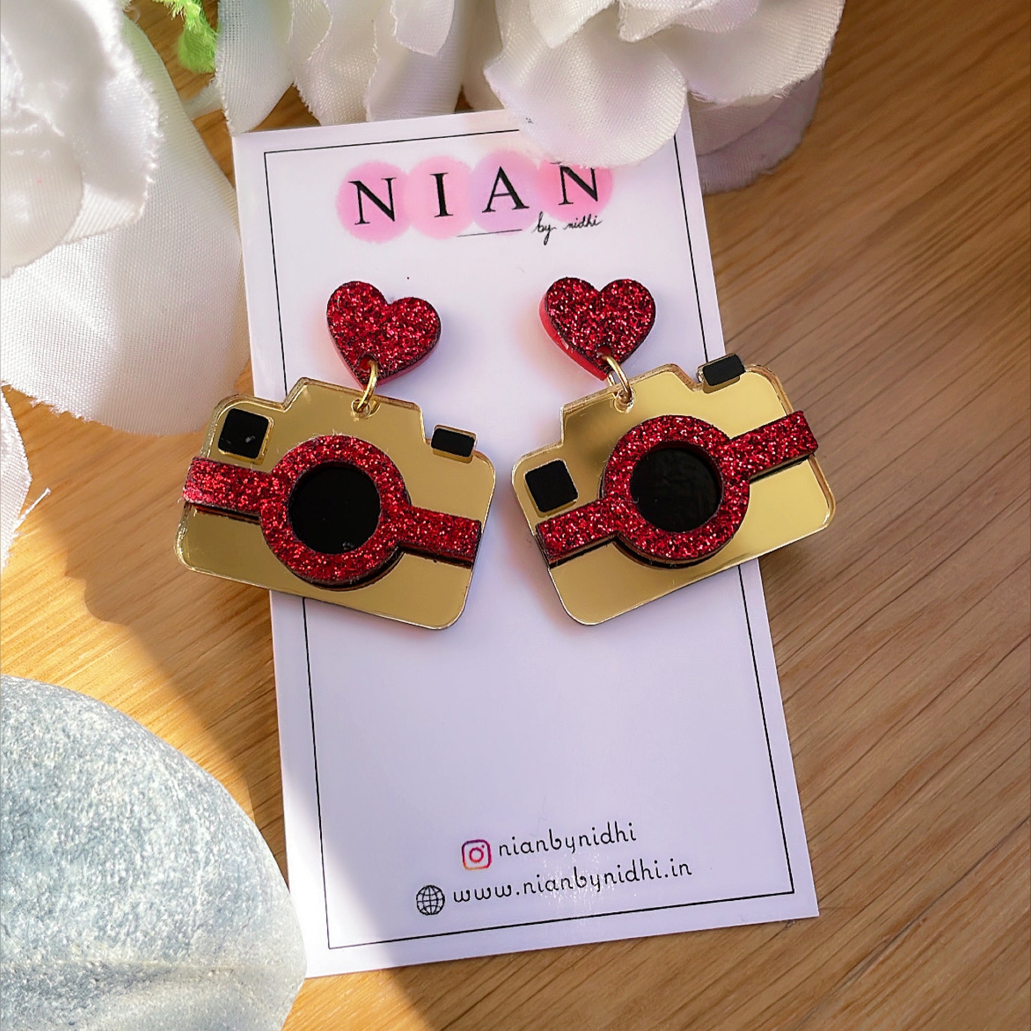 Camera Earrings - Multicolor - Glossy Golden and Shimmer Red - Nian by Nidhi - placed in a white and brown background