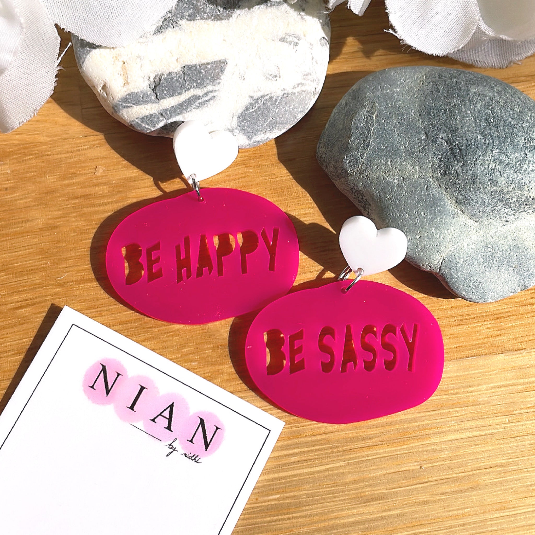 Be Happy Be Sassy Earrings - Pink and White - Nian by Nidhi - placed in a brown, white, and grey background