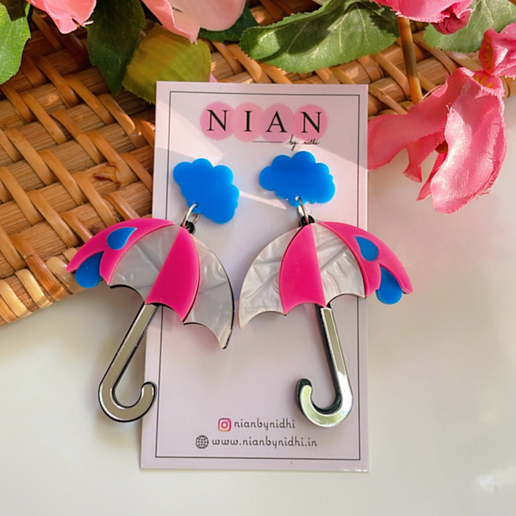 Drizzly Umbrella Earrings - Pink, White and Blue - Nian by Nidhi - placed in a brown, white, and pink background