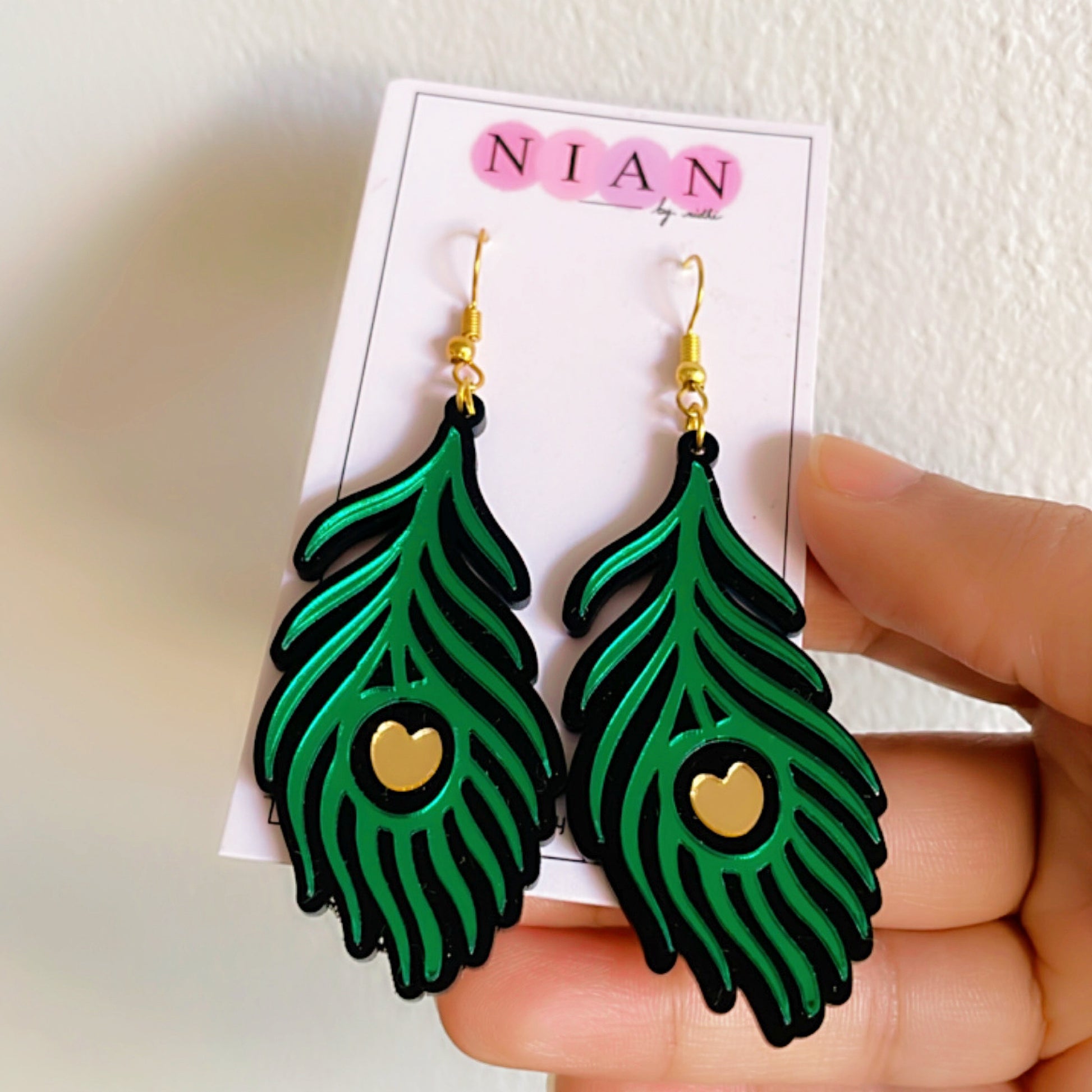 Morpankh Danglers - Glossy Green with Black and Golden details - Nian by Nidhi - placed in a white background and held in a hand