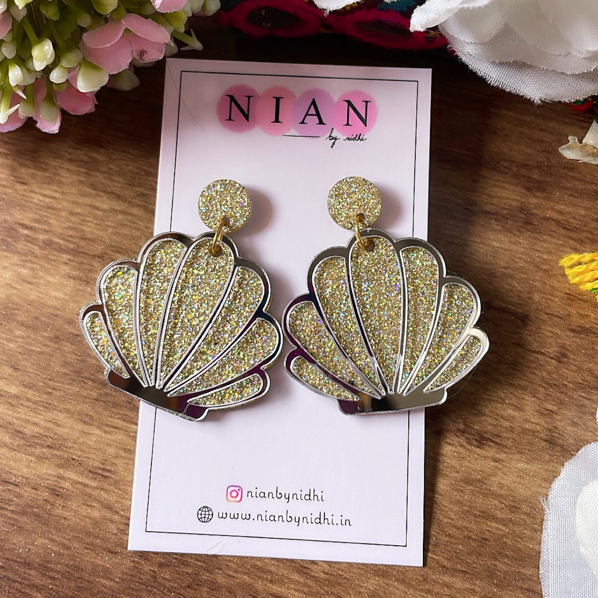 Shiny Shell Earrings - Nian by Nidhi - Shimmer Golden and Glassy Silver - placed in a brown and colorful background