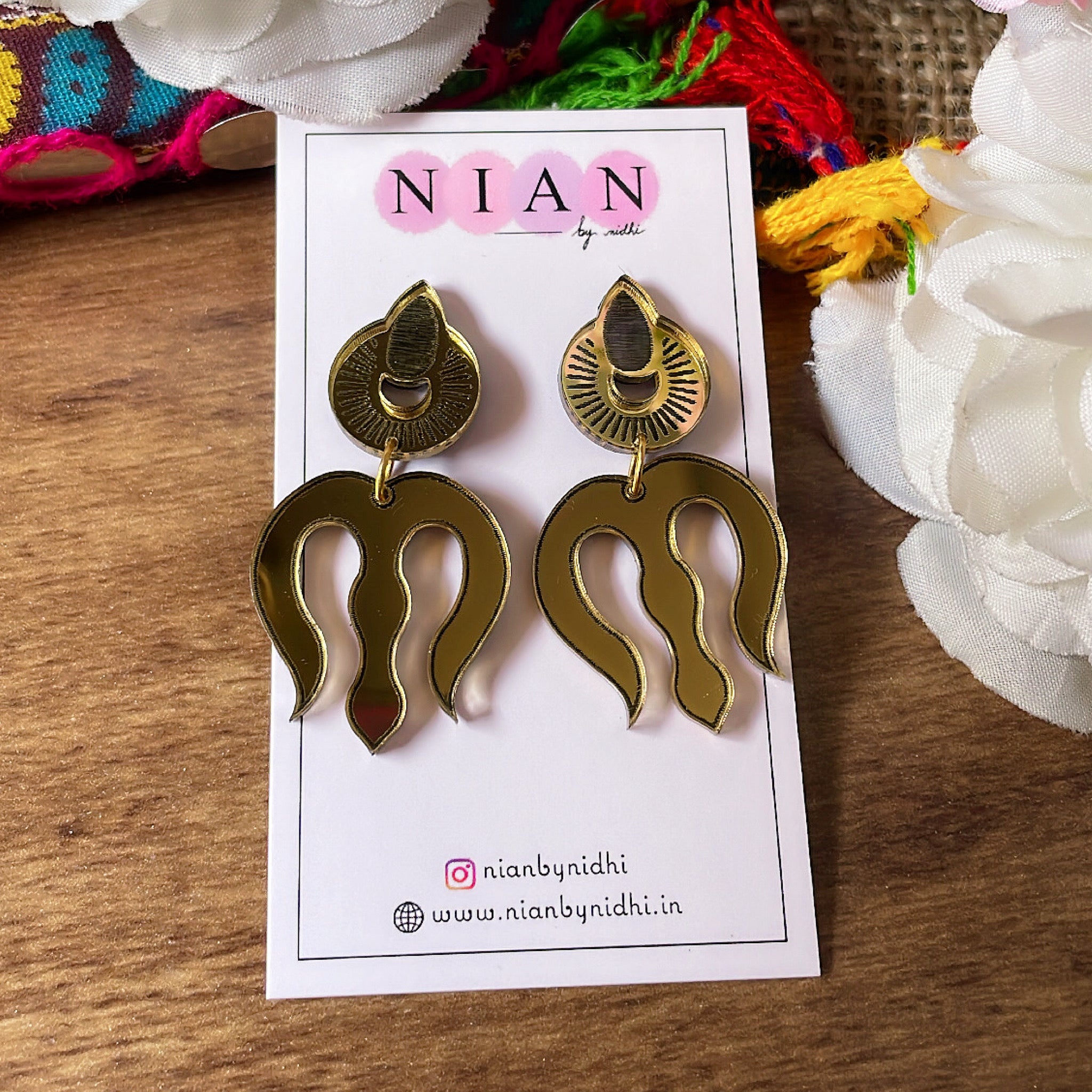 Trishul Earrings - Nian by Nidhi - Glassy Golden - placed in a brown and colorful background