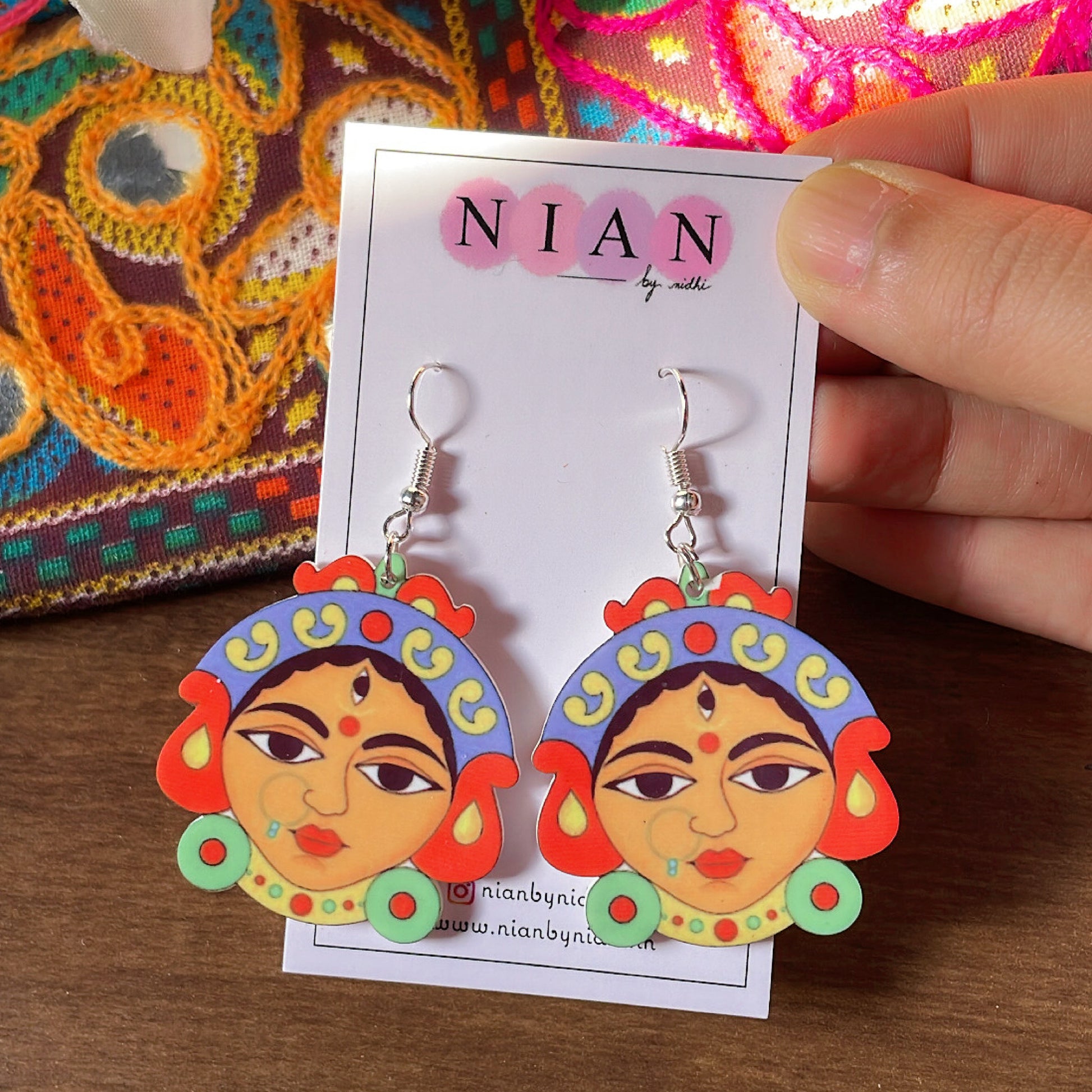 Durga Maa Earrings - Nian by Nidhi - Multicolor - held in a hand, placed in a colorful brown background