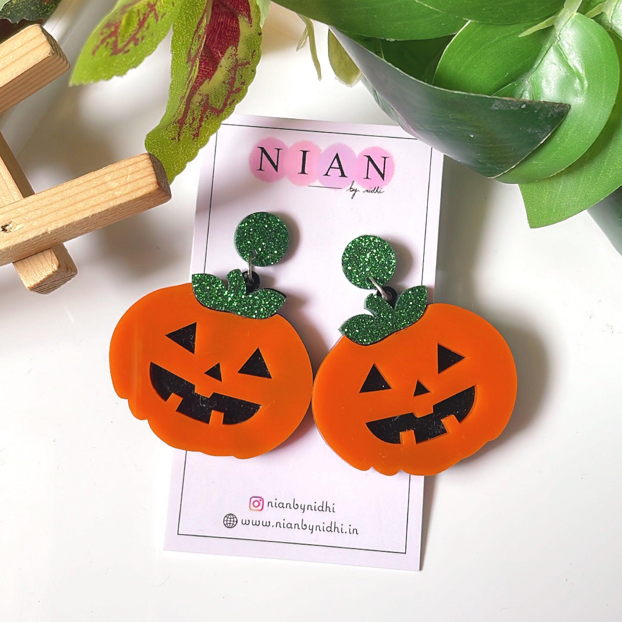 Plumpy Pumpkin Earrings - Orange, Black and Shimmer Green - Nian by Nidhi - placed in a white and green background