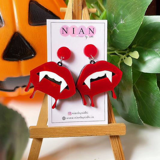 Bloody Lips Earrings - Red and White - Nian by Nidhi - placed on a small wooden canvas in a background that contains a halloween pumpkin and some leaves