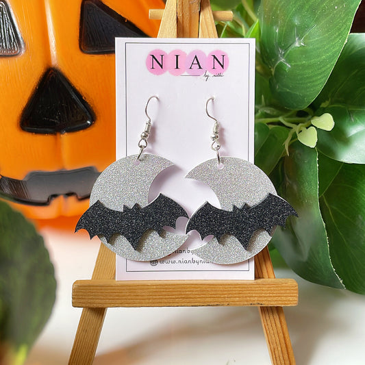 Spooky Night Earrings - Shimmer Silver and Shimmer Black - Nian by Nidhi - placed on a small wooden canvas in a background that contains a halloween pumpkin and some leaves