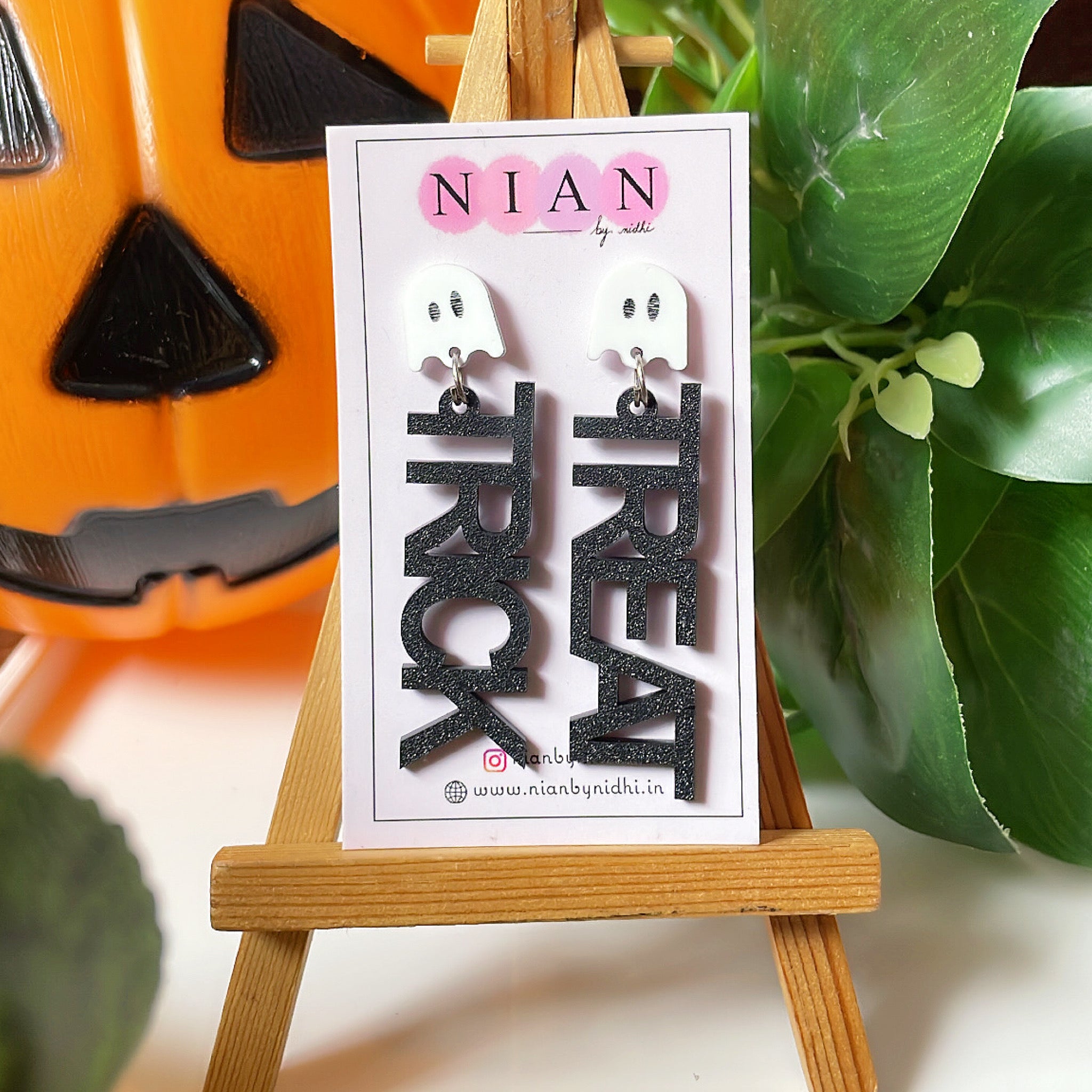 Trick or Treat Danglers - White and Shimmer black - Nian by Nidhi - placed on a small wooden canvas in a background that contains a halloween pumpkin and some leaves
