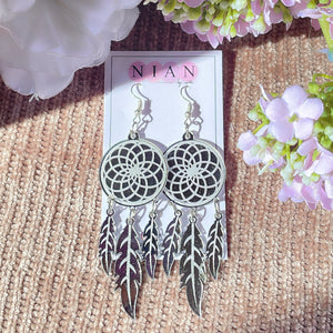 Dreamcatcher Earrings - Glossy Silver with embossing - Nian by Nidhi - placed in a light brown and light pink background