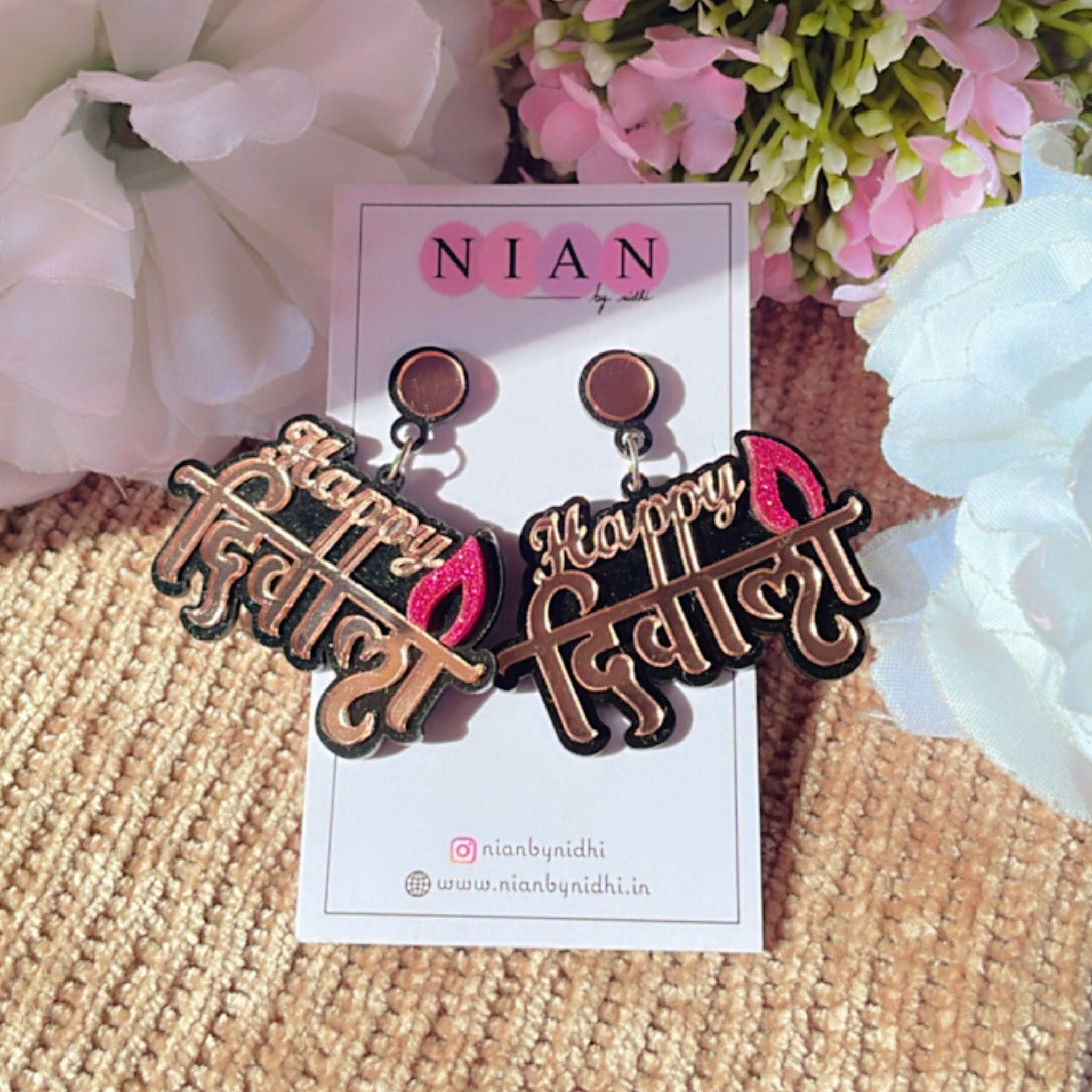 Happy Diwali Earrings - Rosegold and Pink on Black base - Nian by Nidhi - placed in a light flowery background
