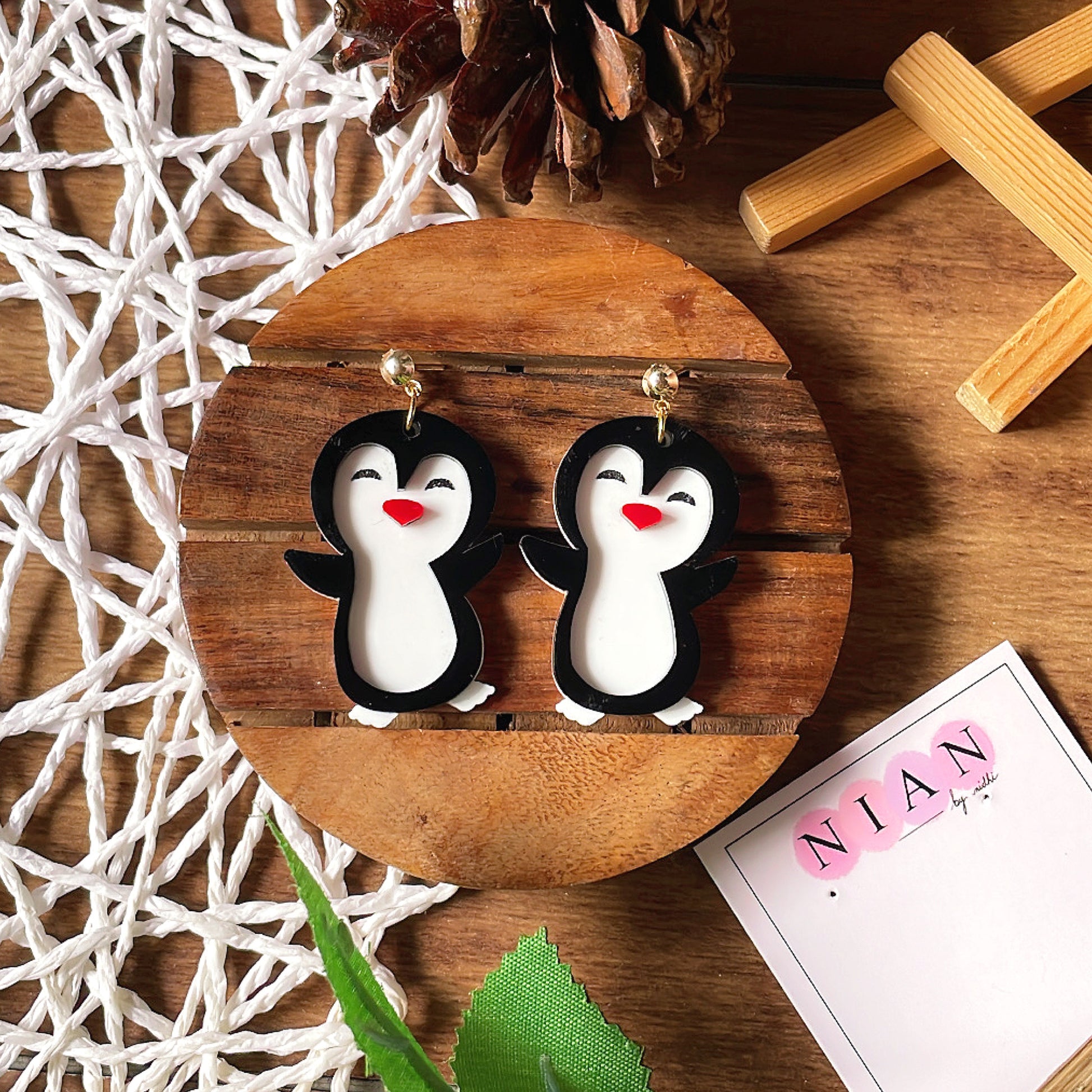 Punny Penguin Earrings - White, Black and Red - Nian by Nidhi - placed in a brown and white background