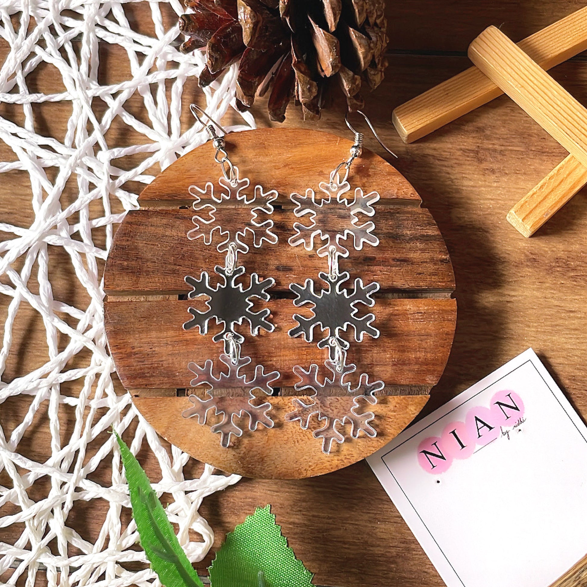 Snowflake Danglers - holographic, glassy blue, and silver - Nian by Nidhi - placed in a white and brown background with a Nian by Nidhi Earring card