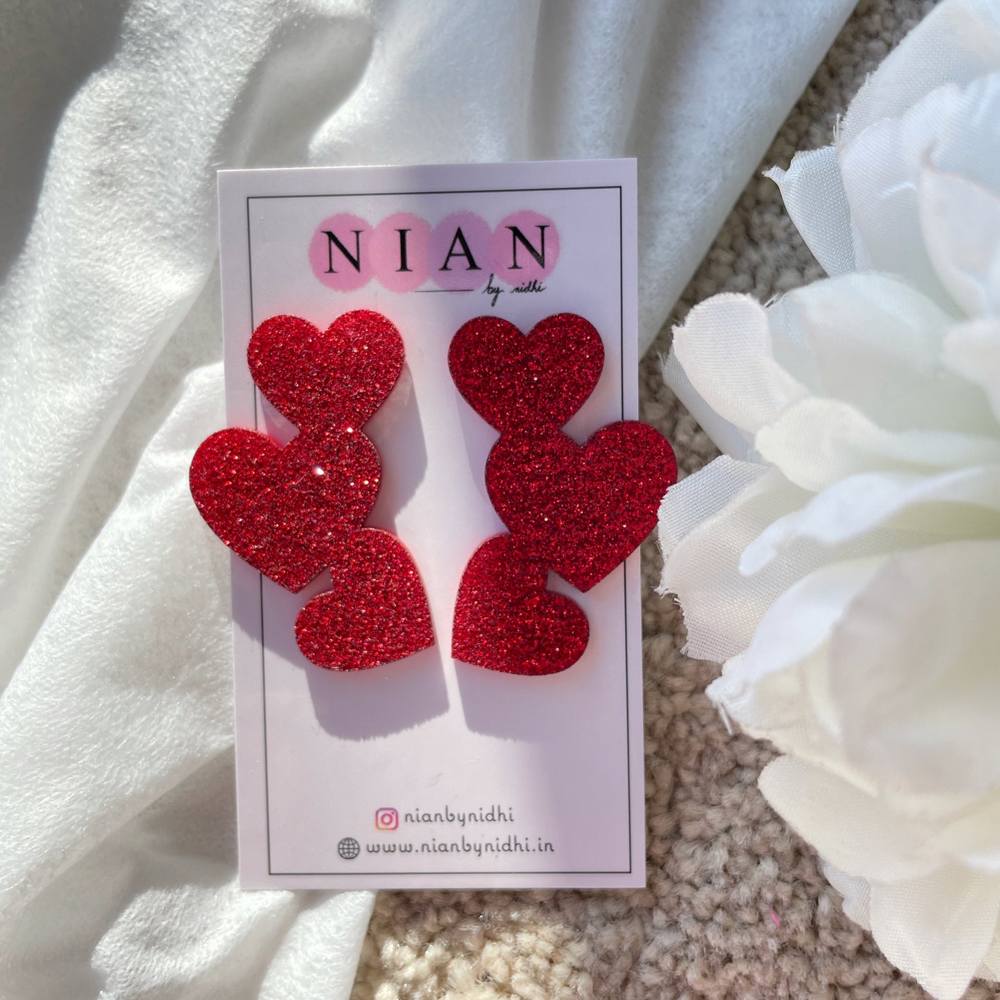 Tri Heart Earrings - made of 3 shimmering Red hearts - Nian by Nidhi - in a white background, placed on Nian by Nidhi Earring cards