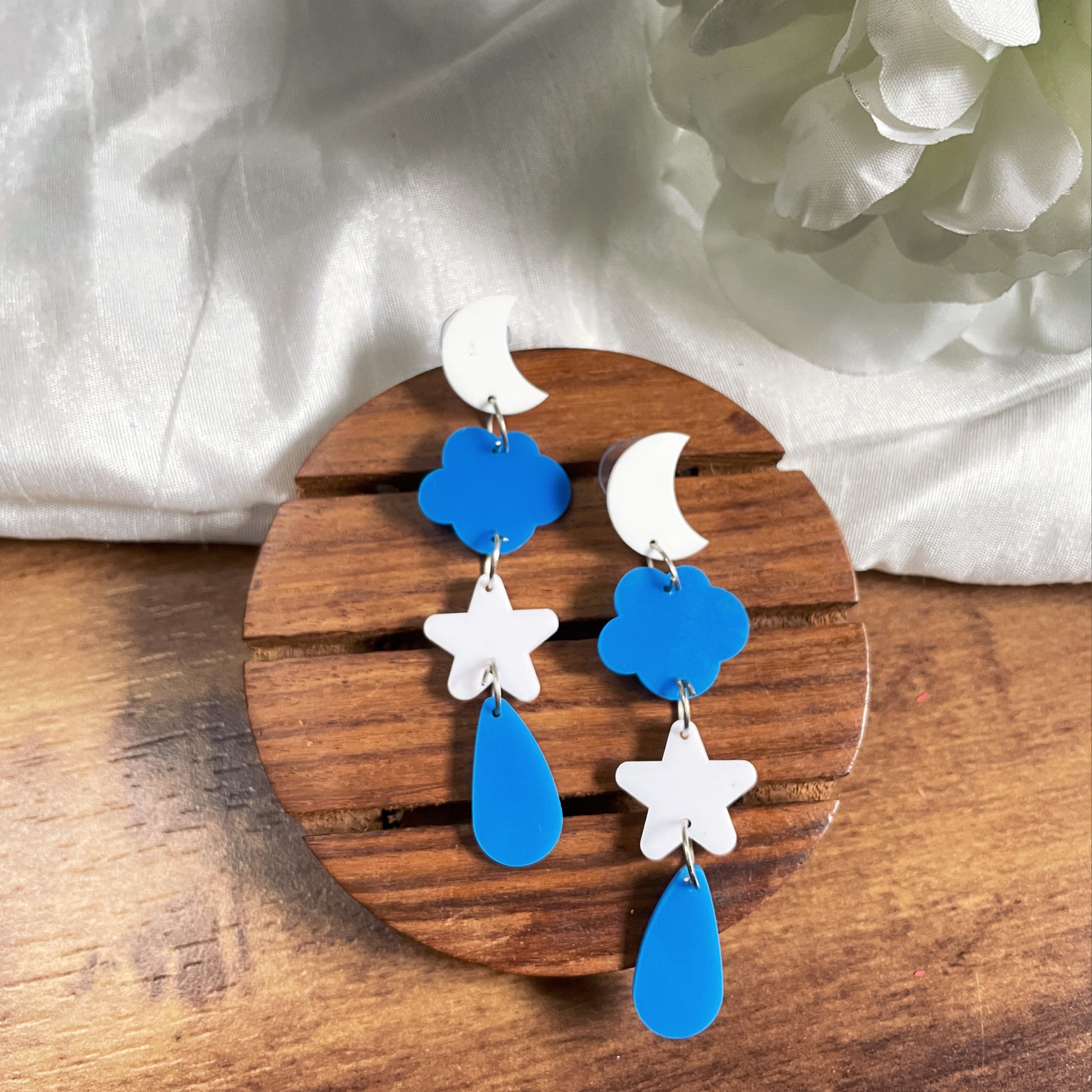 Galaxy Earrings - Blue and White consisting of stars, clouds, moon, and raindrops - Nian by Nidhi - in a white and brown background