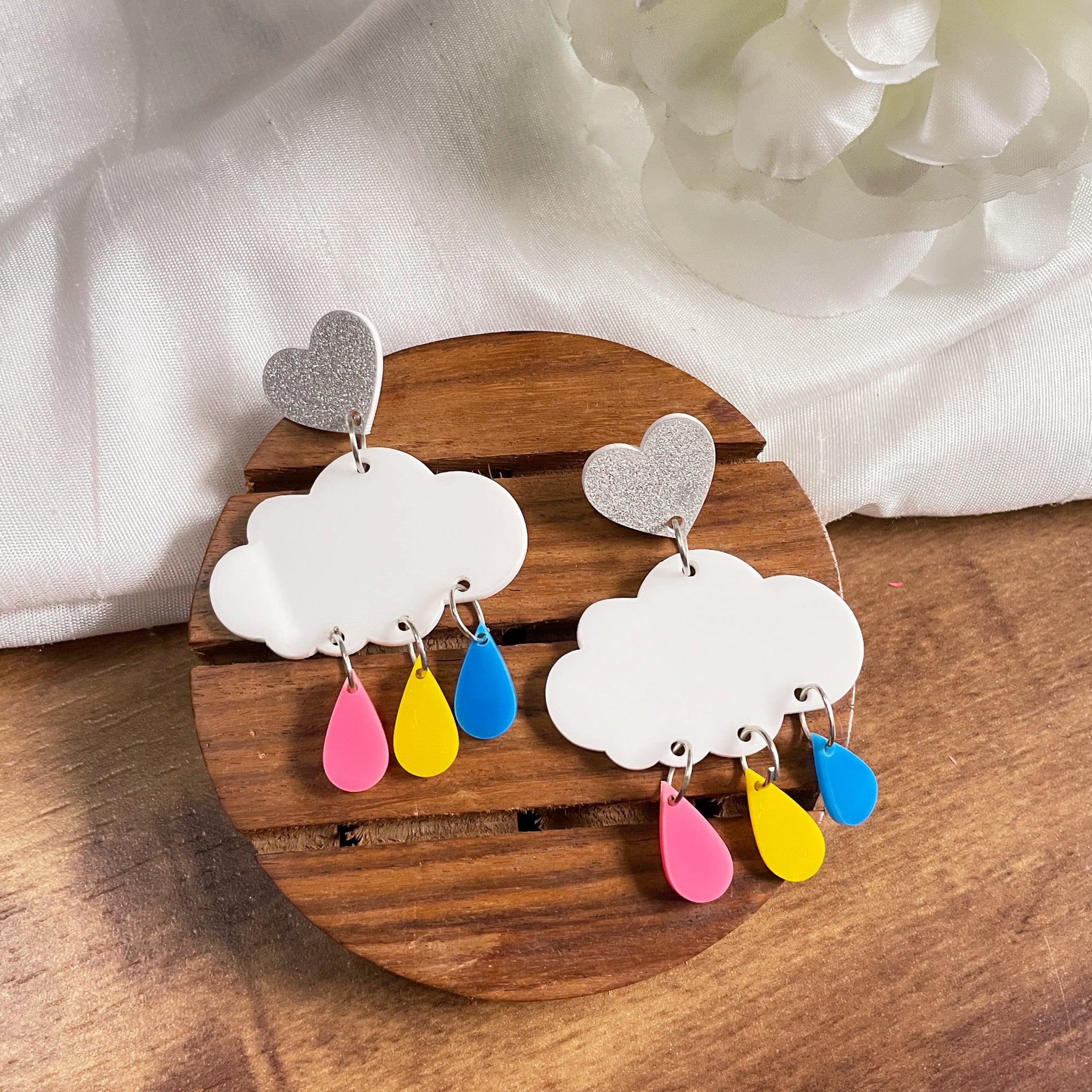 Rainy Cloud Earrings - multi color - Pink, Yellow, and Blue, with white clouds and silver hearts - Nian by Nidhi - in a white and brown background