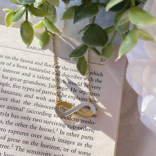 Infinity Necklace - Glossy Golden and Silver - Nian by Nidhi - placed in a white and green background, placed on a book