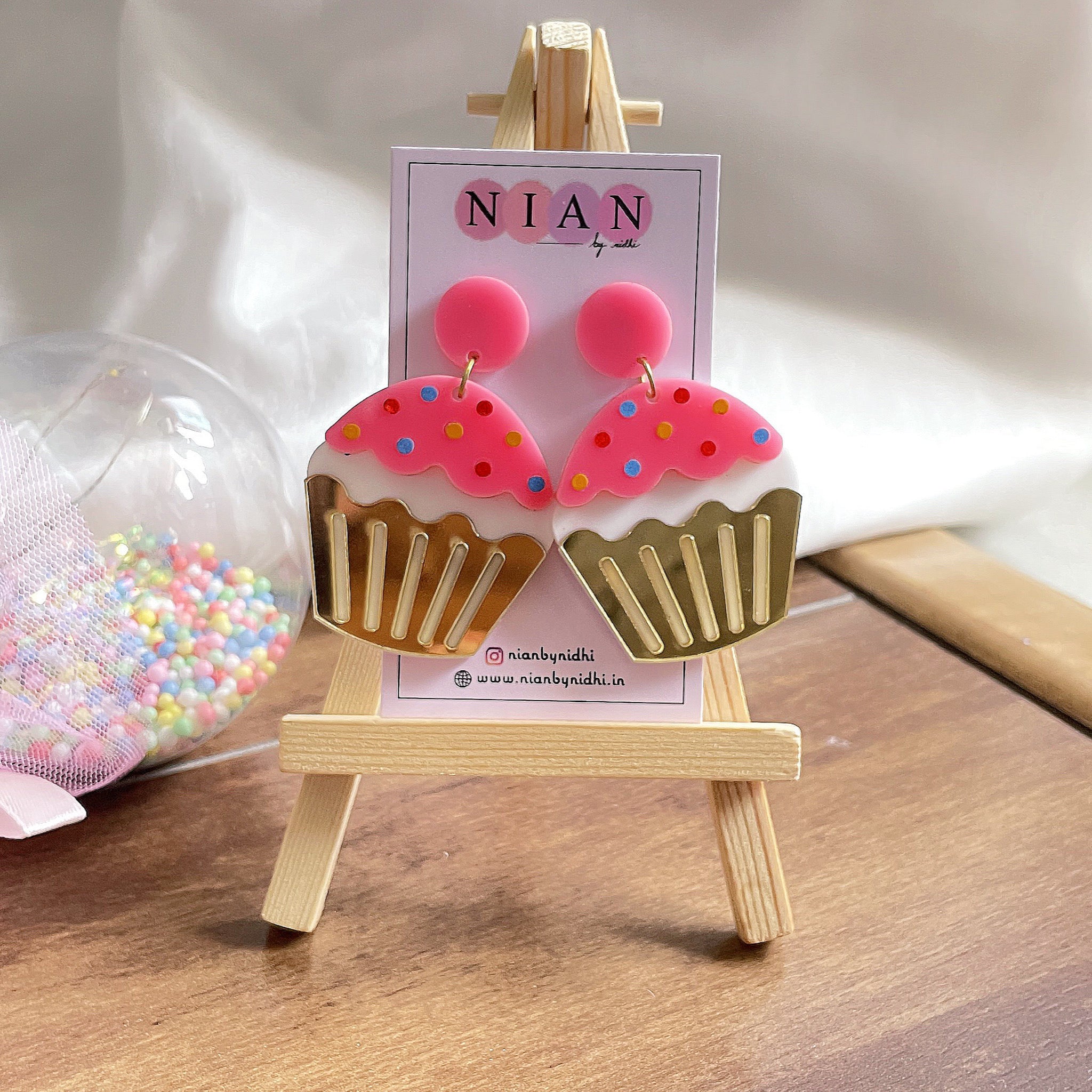 Cupcake Earrings - Pink, White, and Golden - Nian by Nidhi - in a white and brown background, placed on a small wooden canvas with Nian by Nidhi's earring card