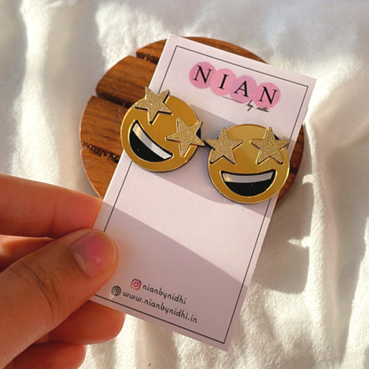 Star-Struck Emoji Studs - Golden with face detailings - Nian by Nidhi - placed in a brown and white background