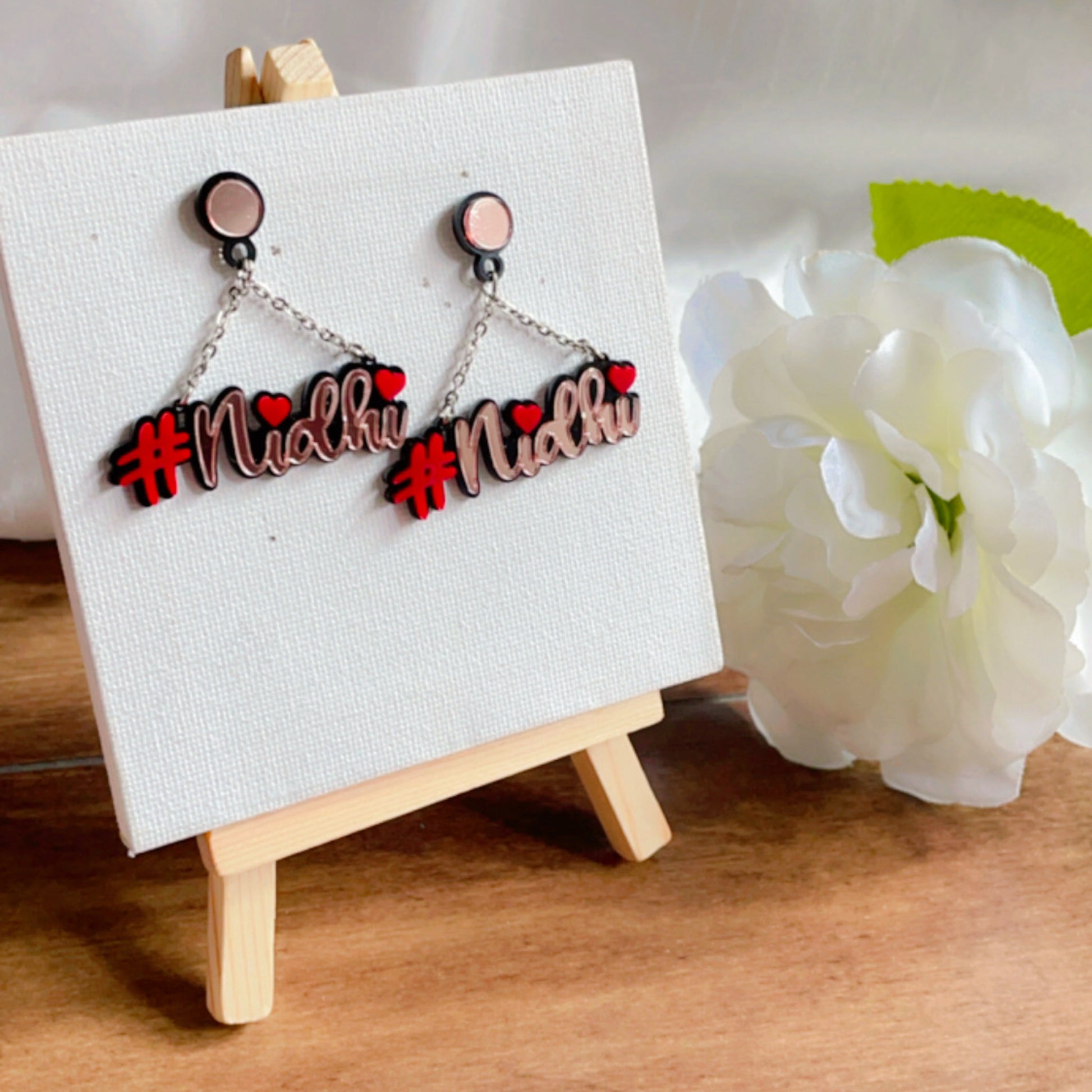 Customised Alphabet Earrings - personalised with a text - #nidhi - red and rose gold - Nian by Nidhi - placed on a small plain white canvas - in a white flowery background