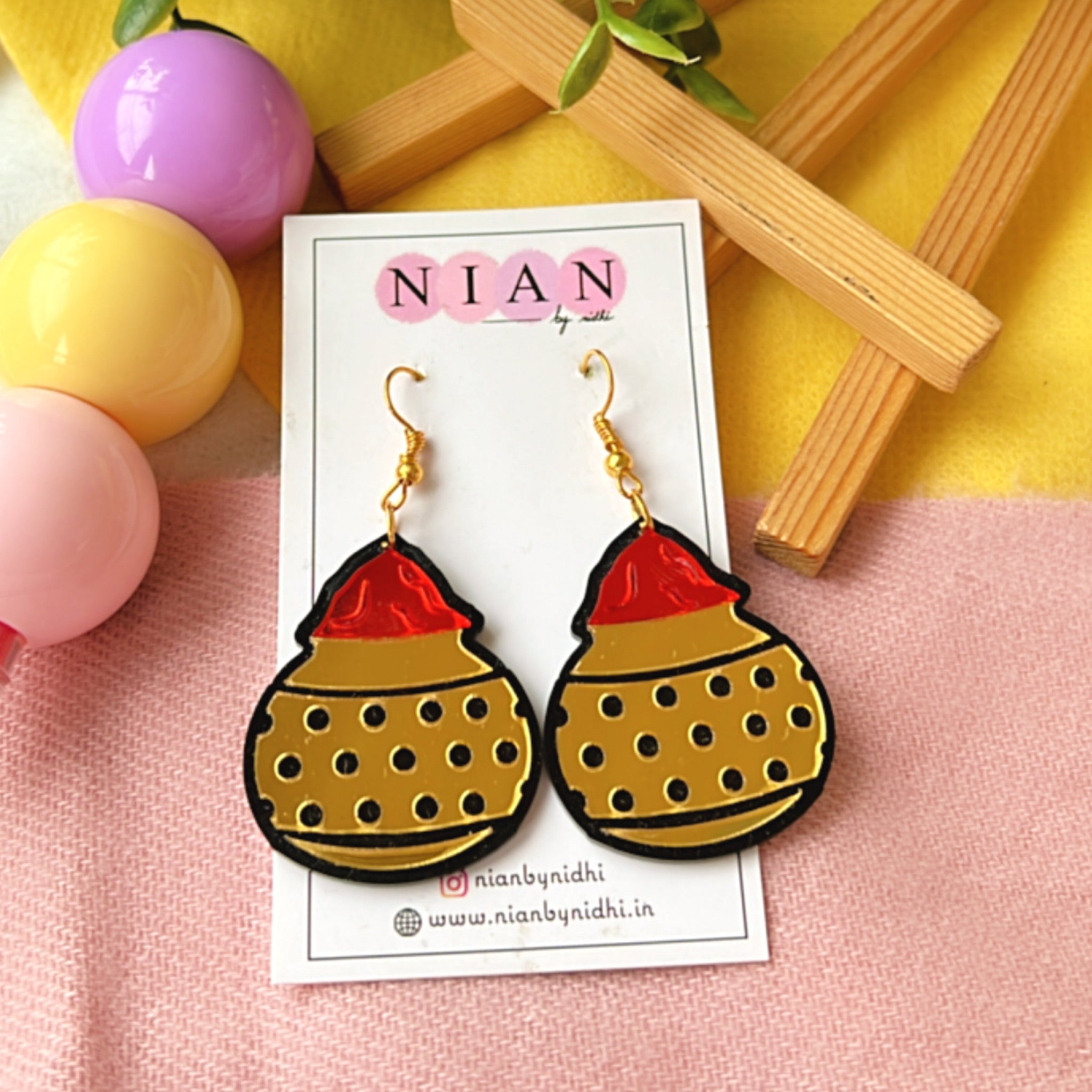 Gulal ki Matki Earrings - Glossy Golden and Red - Nian by Nidhi - placed in a colorful background