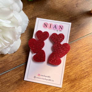 Tri Heart Earrings - made of 3 shimmering Red hearts - Nian by Nidhi - in a white and brown background, placed on Nian by Nidhi Earring cards