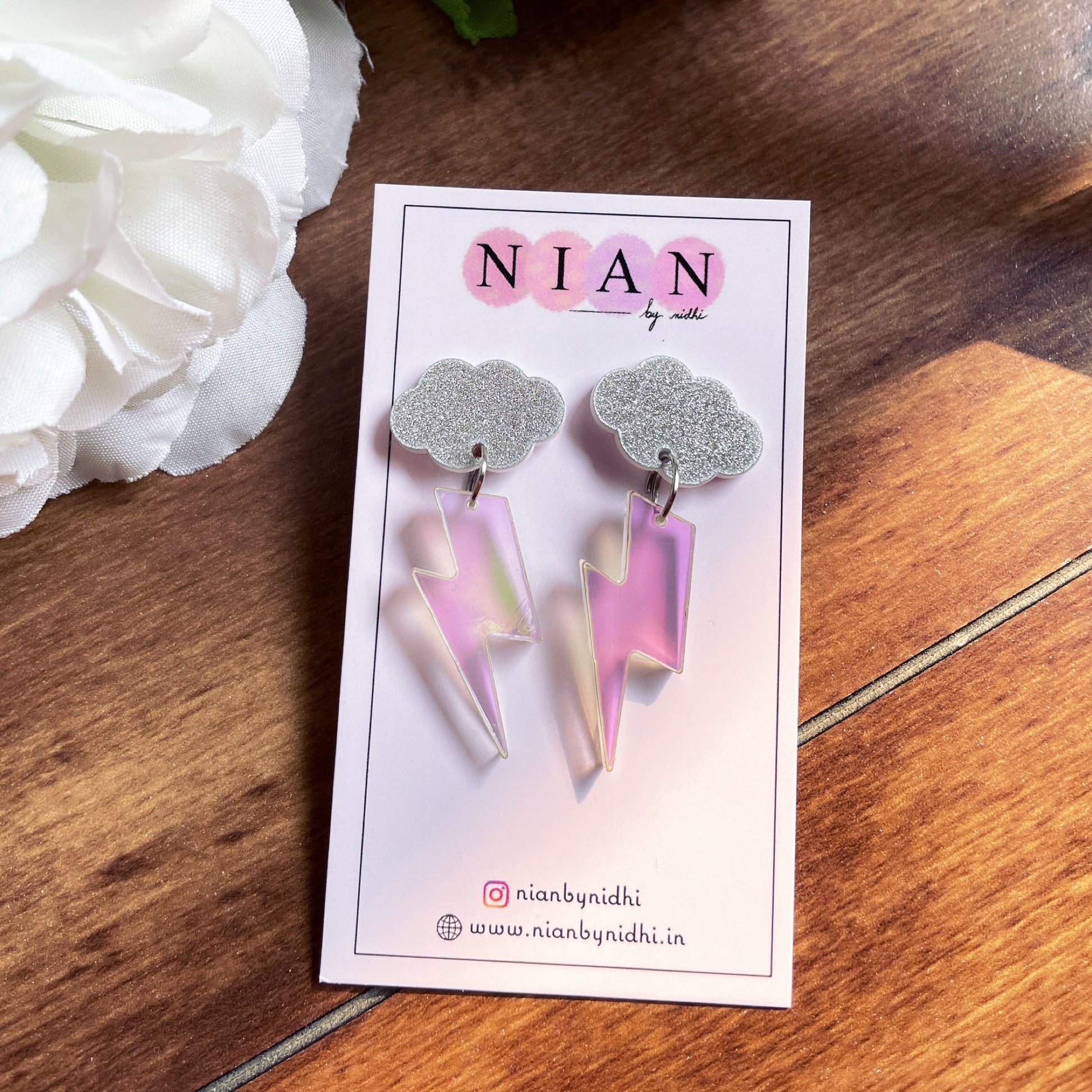 Thunder Cloud Earrings - Holographic and silver with shimmer - Nian by Nidhi - placed on a Nian by Nidhi earring card - in a brown background