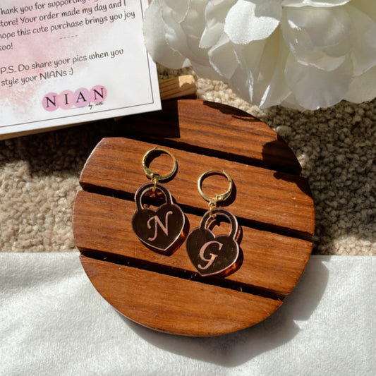 Initial Heart Lock Earrings - Glossy Rosegold - Nian by Nidhi - placed in a white and light beige background