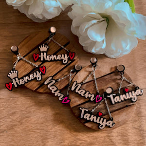 A collection of several Customised Alphabet Earrings - personalised with a various texts - "Honey", "Nam", "Taniya" - red or pink and rose gold - Nian by Nidhi - in a white and brown background