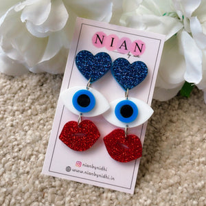 Evil Eye Charm Earrings - Shimmer blue, red and white - Nian by Nidhi - placed in a light beige background