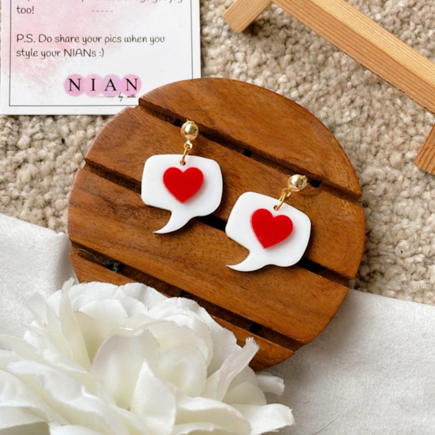 Message from Heart Earrings - Nian by Nidhi - White and Red - placed in a brown and white background with a flower