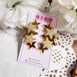 Glitter Star Earrings - Nian by Nidhi - Golden and Glitter Golden - placed in a white flowery background