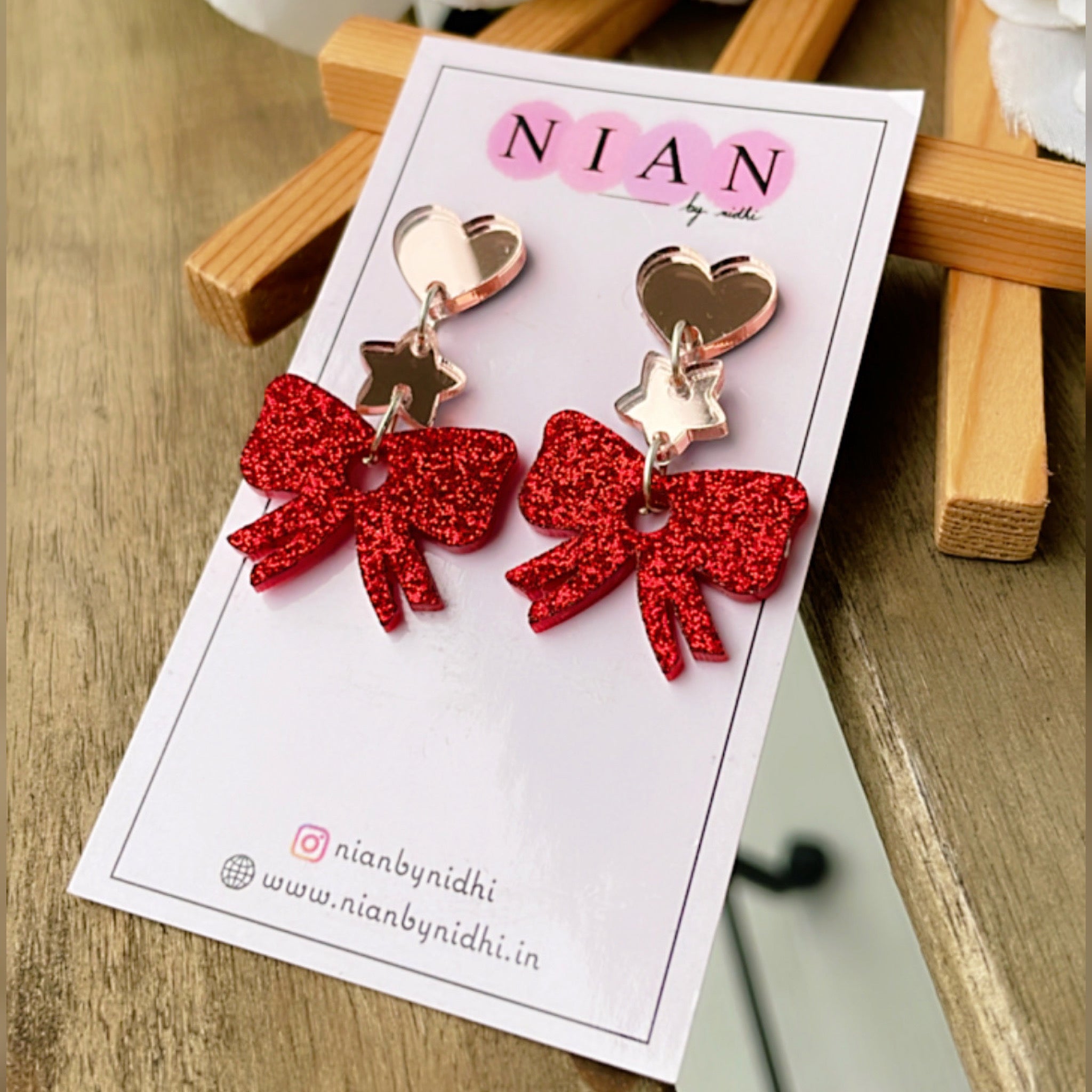 Bow Danglers - Shimmer Red and Rosegold - Nian by Nidhi - placed in a brown background