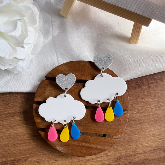 Rainy Cloud Earrings - multi color - Pink, Yellow, and Blue, with white clouds and silver hearts - Nian by Nidhi - in a white and brown background, as well as a plain white canvas