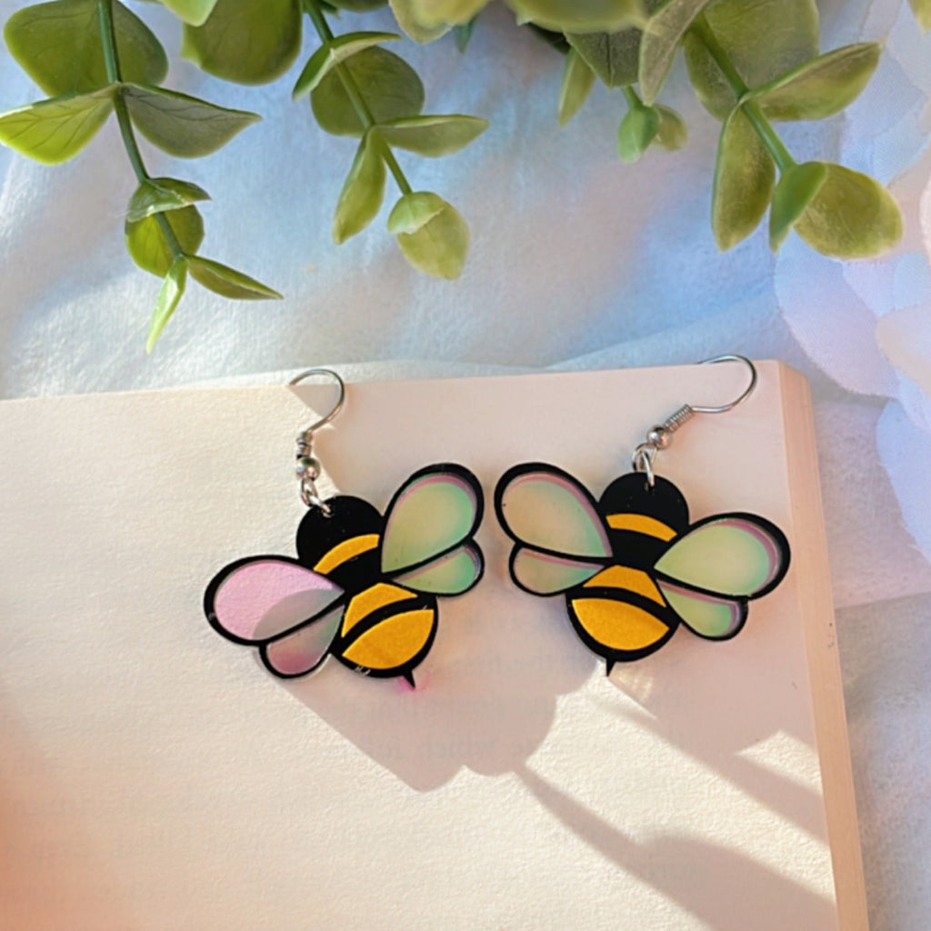 Baby Bee Earrings - Yellow and Black with a Holographin Effect - Nian by Nidhi - placed in a white and green background
